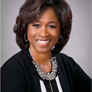 A woman in a black top and silver necklace smiles at the camera.